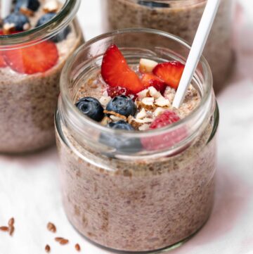 A close up view of a jar of flaxseed pudding with fruit and chopped almonds with a spoon inside.