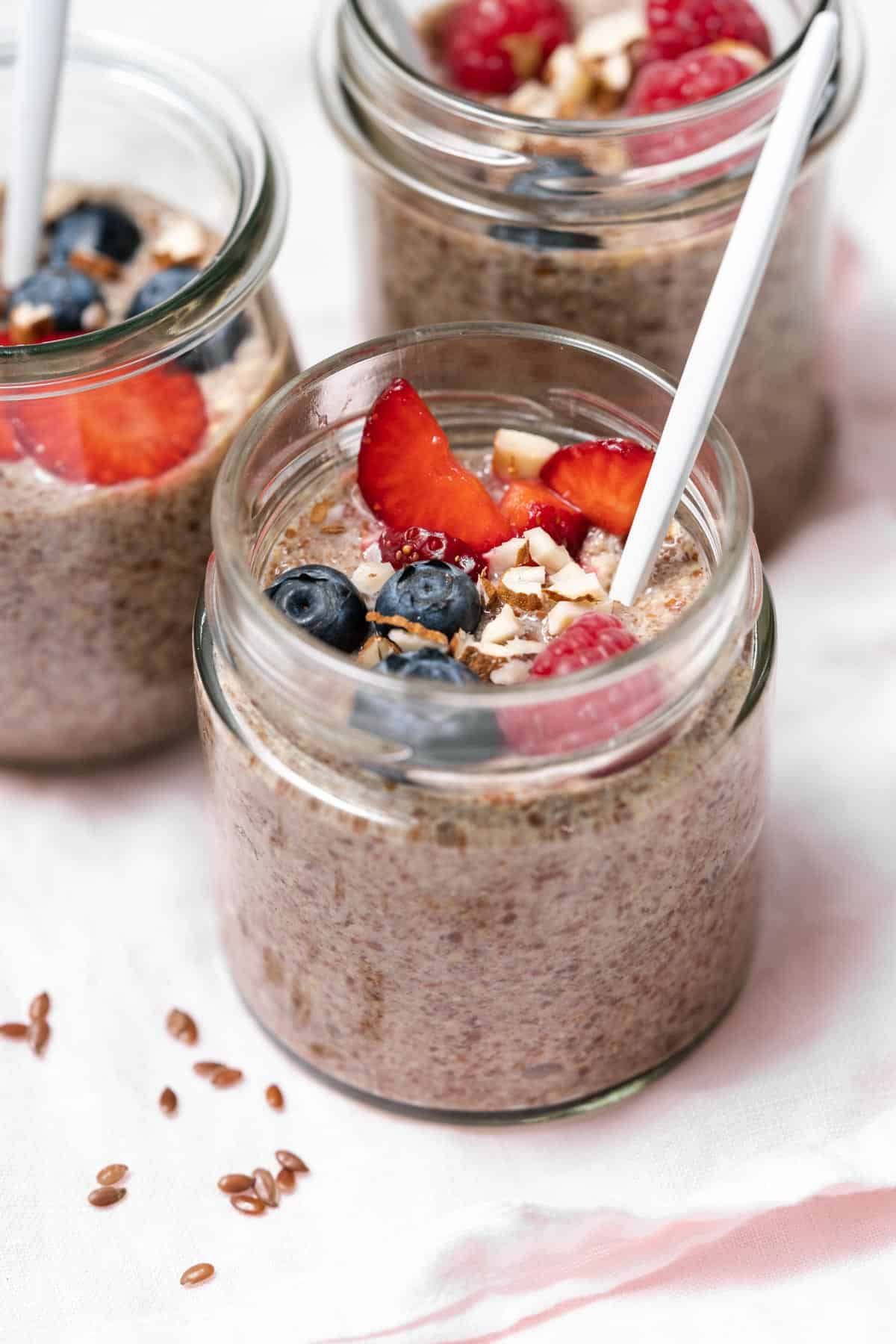 A close up view of a jar of flaxseed pudding with fruit and chopped almonds with a spoon inside.