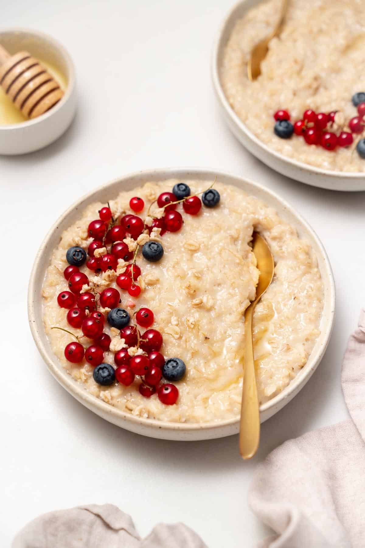 A bowl of honey oatmeal topped with berries with a spoon in the bowl.