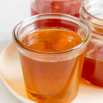 Three jars of hot honey on a plate with one in front.