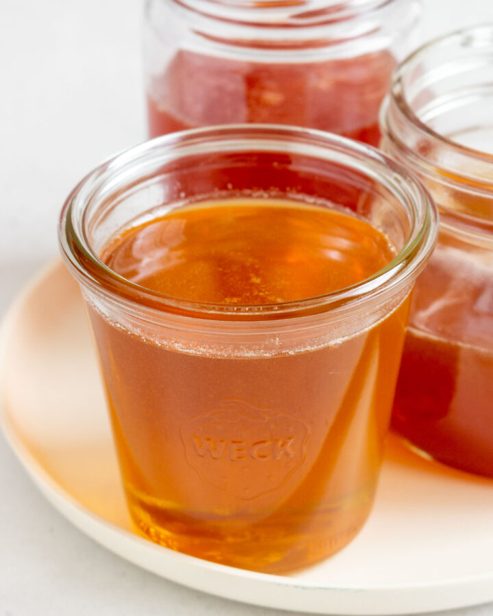 Three jars of hot honey on a plate with one in front.