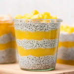 A glass of layered mango chia pudding with diced mangos on top.