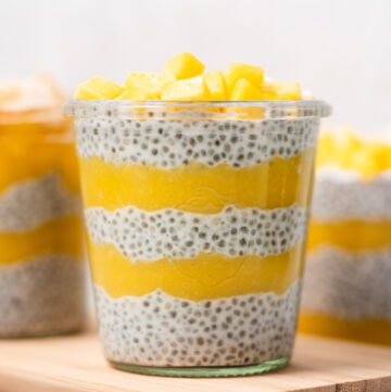 A glass of layered mango chia pudding with diced mangos on top.