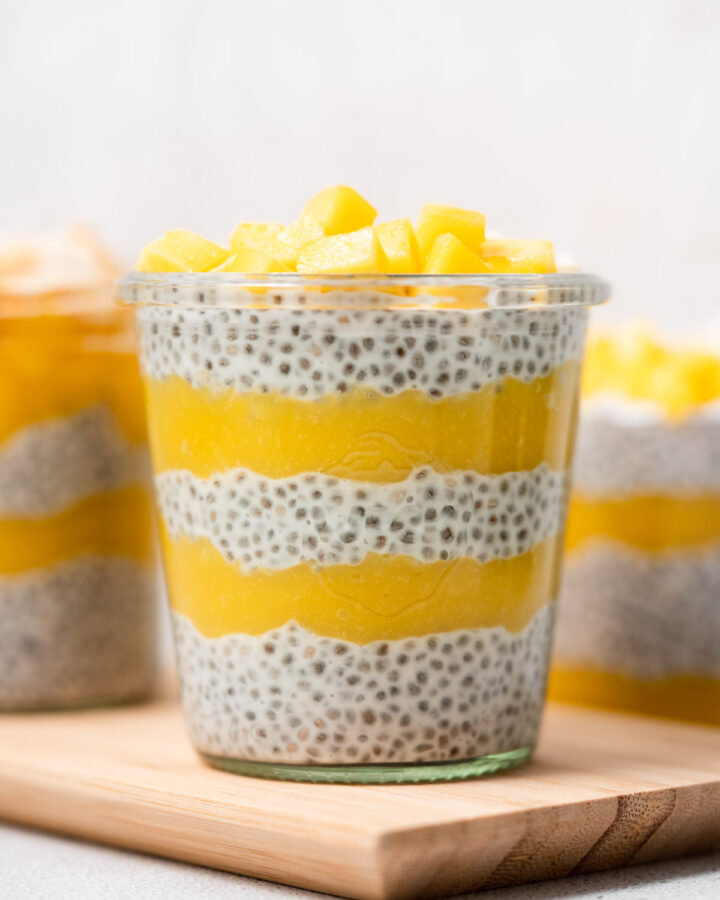 A glass of layered mango chia pudding with diced mangos on top.