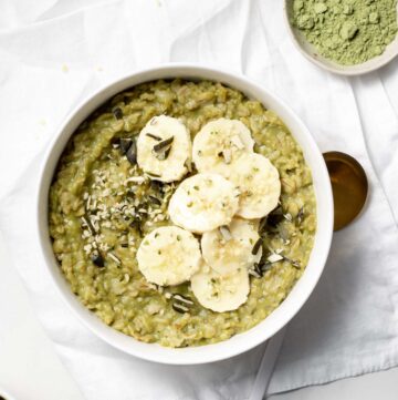 Overhead view of a bowl of matcha oatmeal with sliced bananas and a small bowl of matcha powder on the side.