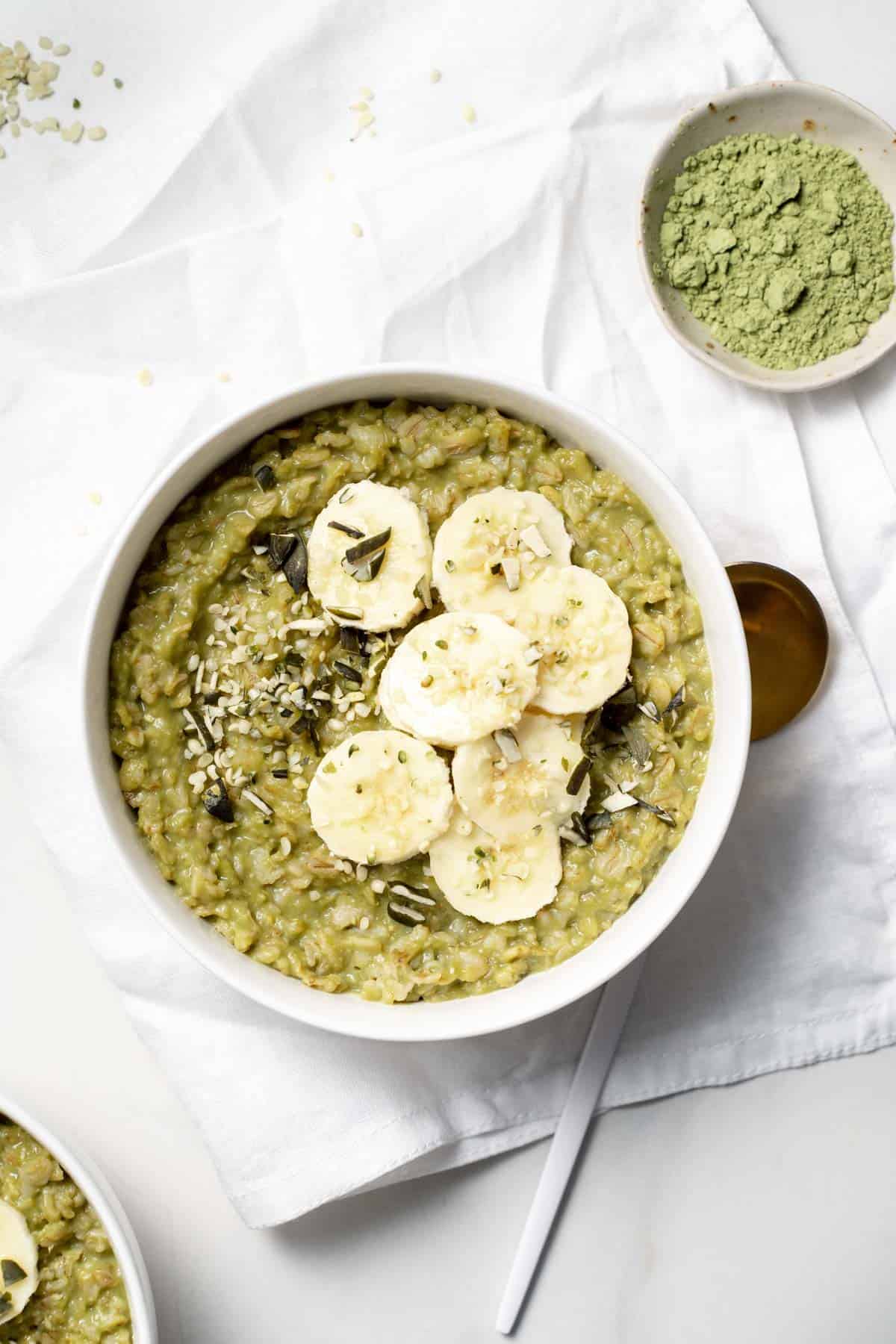 Overhead view of a bowl of matcha oatmeal with sliced bananas and a small bowl of matcha powder on the side.