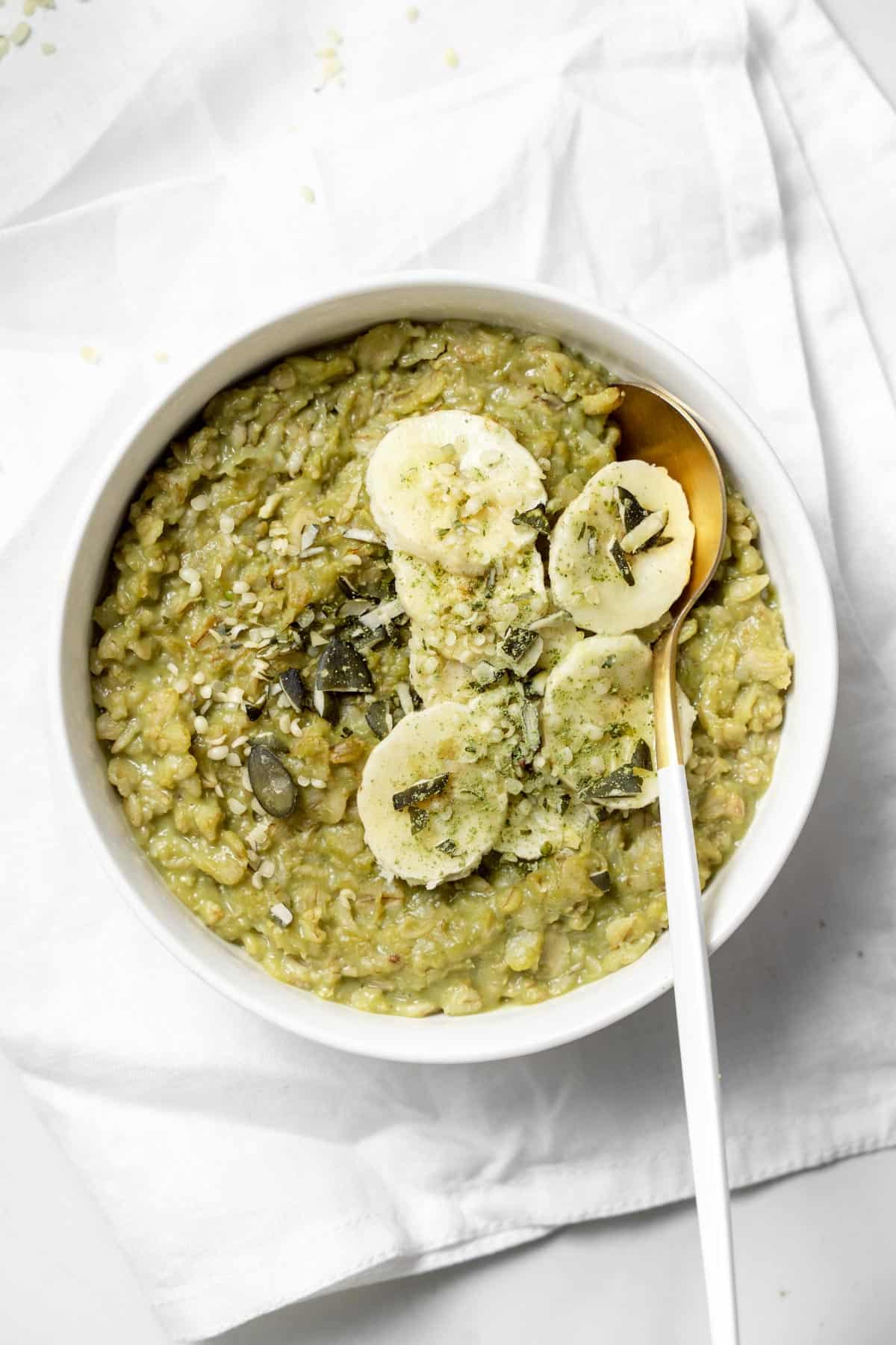 Overhead view of a bowl of matcha oatmeal with sliced bananas and a spoon tucked in.