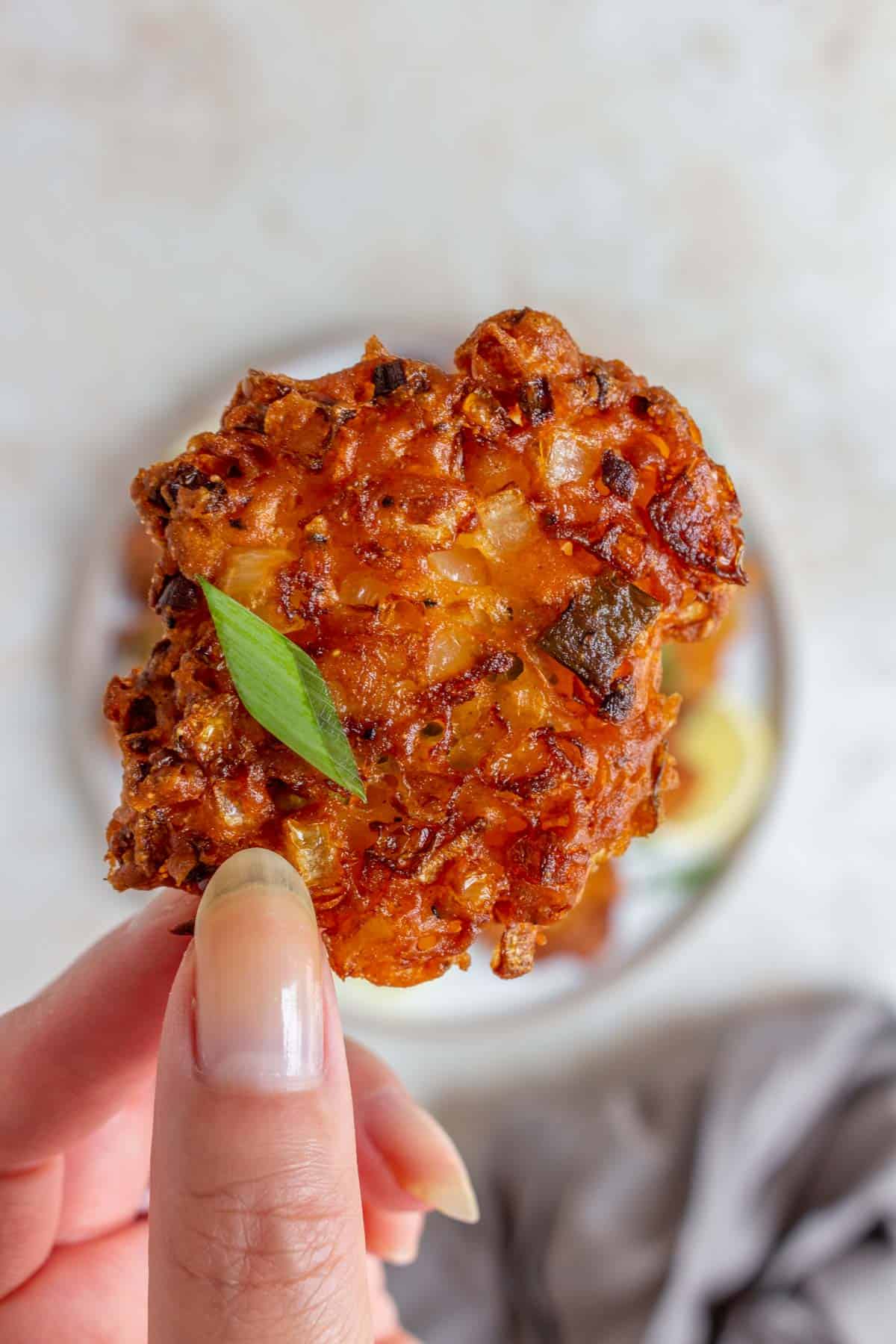 A hand holding up a single crispy onion fritter with a piece of green onion.