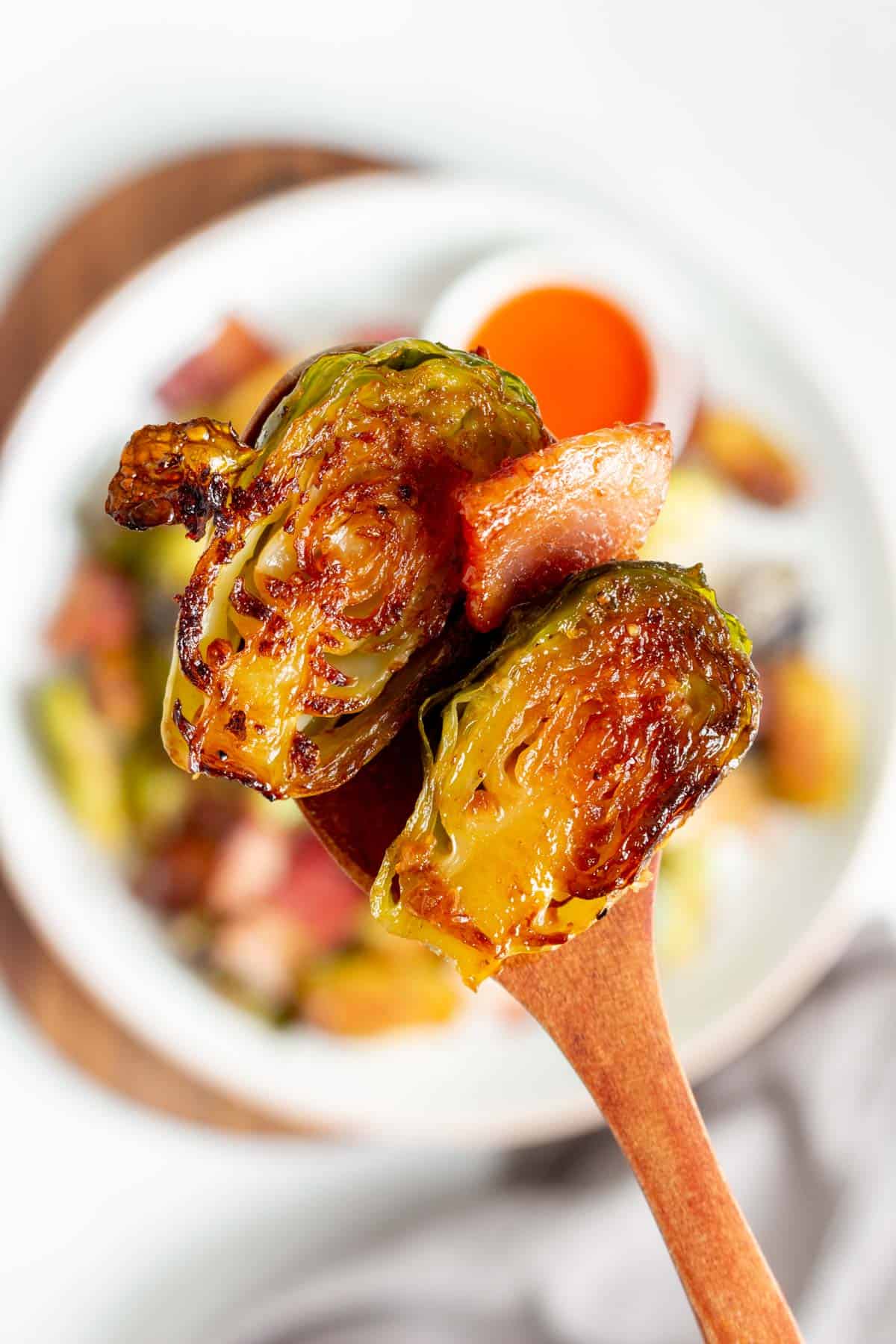 A spoonful of roasted brussels sprouts with bacon lifted from a plate.