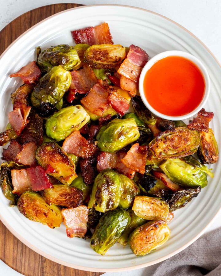 Overhead view of a plate of roasted brussels sprouts with bacon and hot honey with a bowl of hot honey on the side.