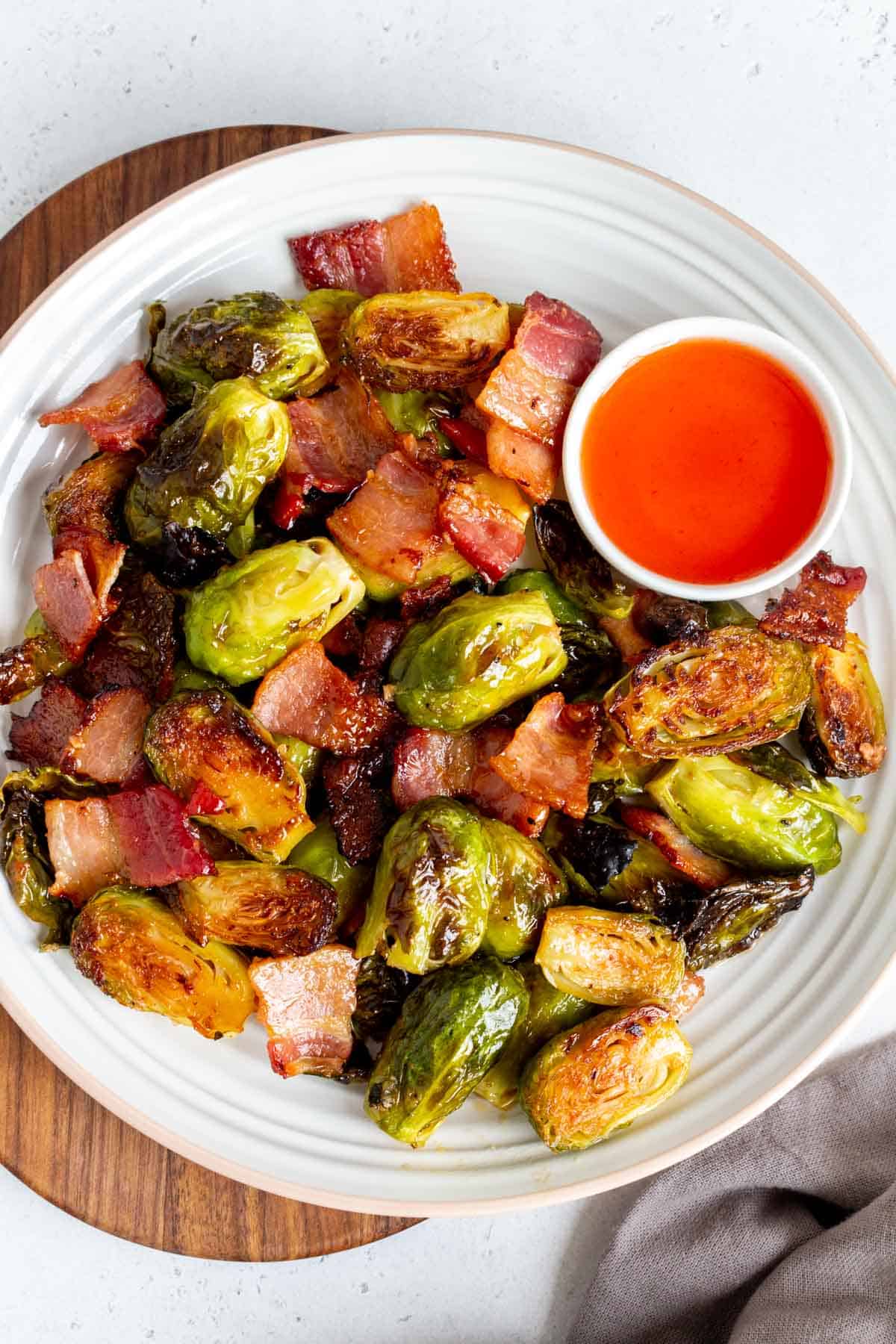 Overhead view of a plate of roasted brussels sprouts with bacon and hot honey with a bowl of hot honey on the side.