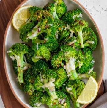 An oval platter of smashed broccoli with red pepper flakes and parmesan on top.