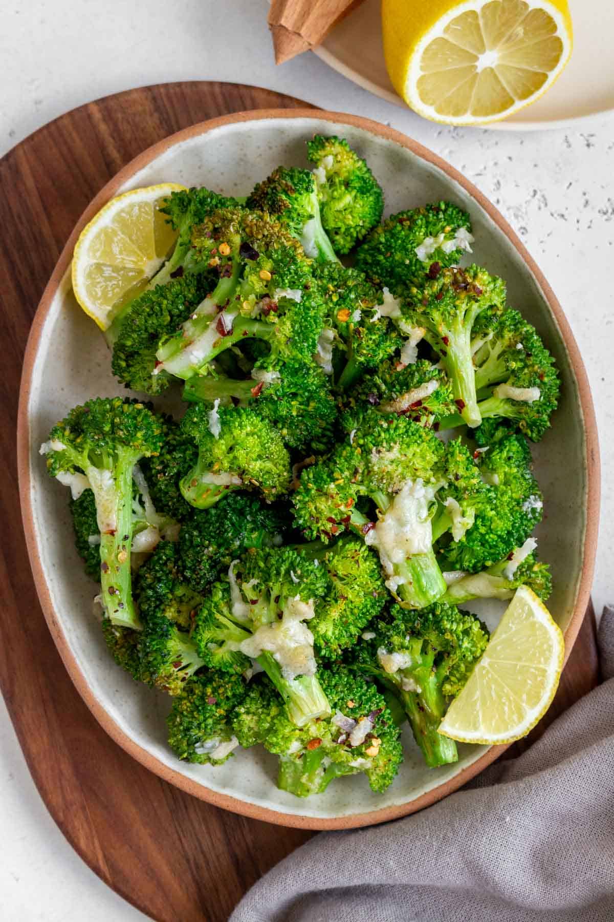 An oval platter of smashed broccoli with red pepper flakes and parmesan on top.