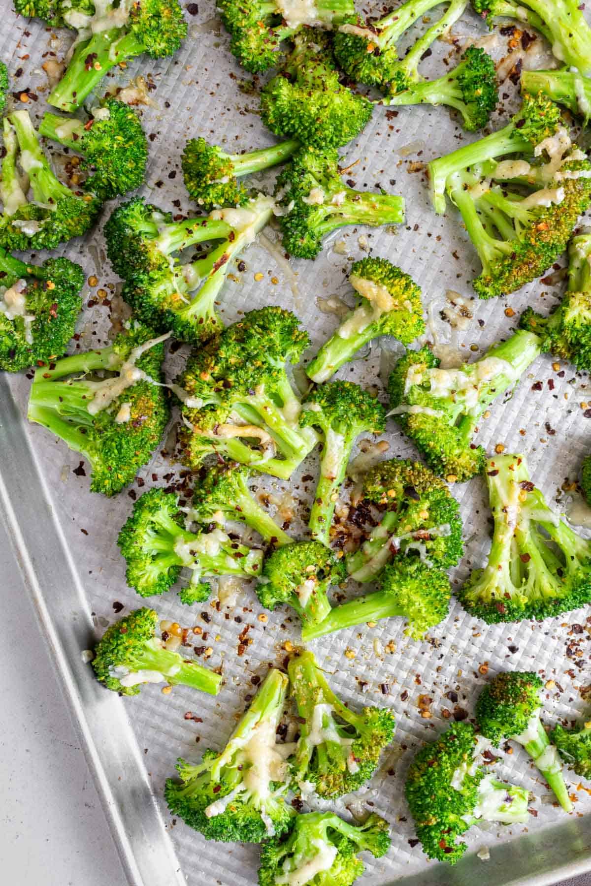 Close up view of a sheet pan of smashed broccoli with parmesan and red pepper flakes.