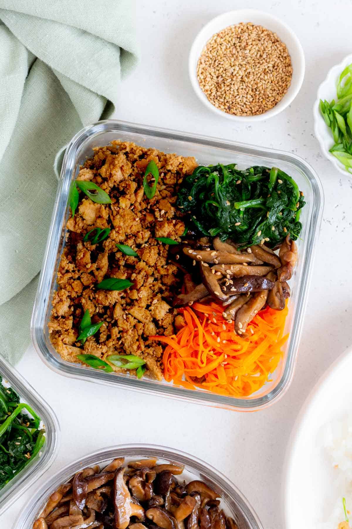 A meal prep container with tofu bulgogi, spinach, mushrooms, and carrots.
