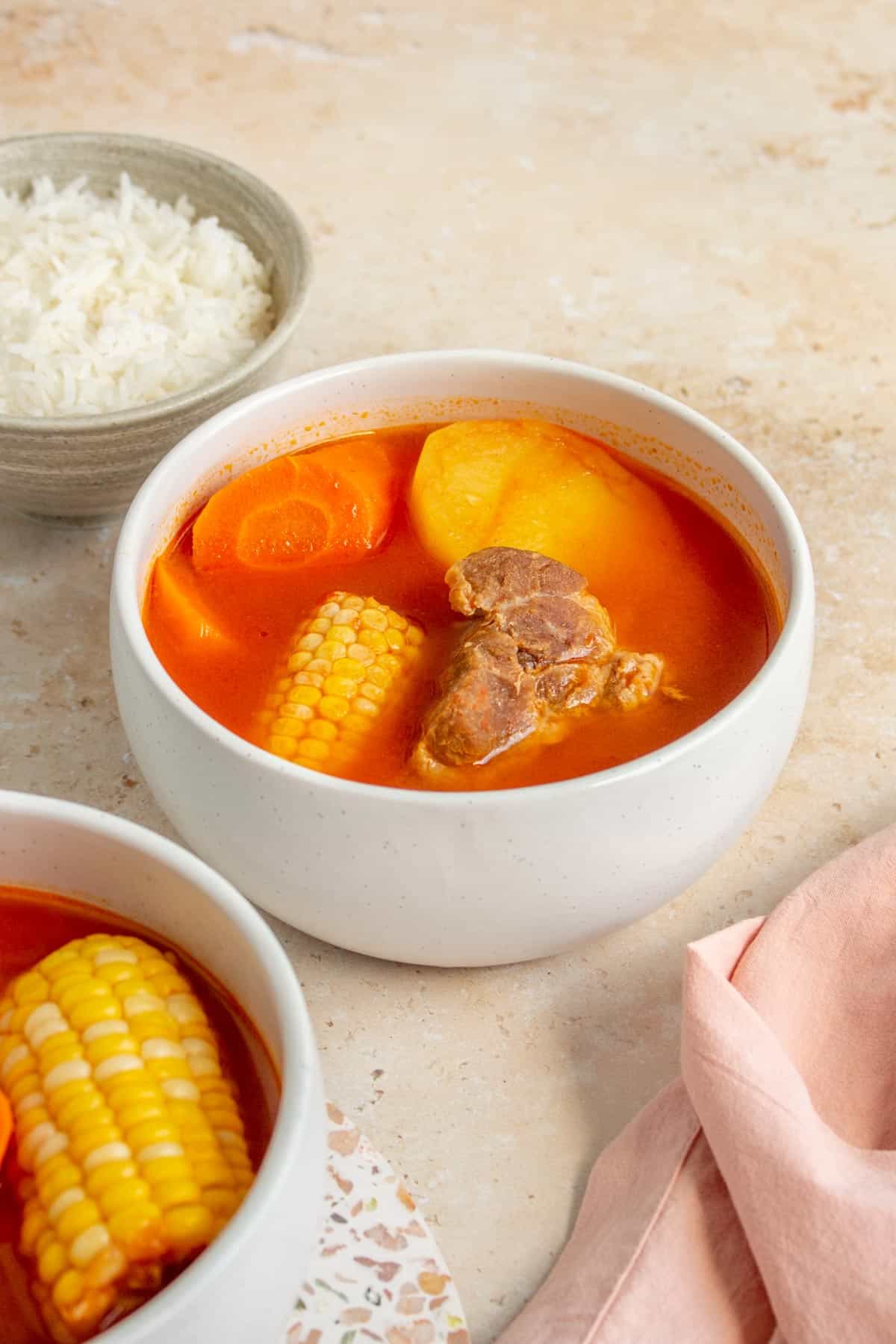 A bowl of ABC soup with pork, corn, potato, and carrot. Rice in the background.