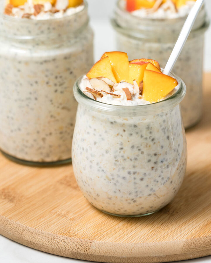Jars of high protein overnight oats topped with peaches on a wooden serving board.