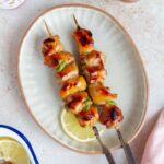 A plate with two yakitori on a skewer with a slice of lemon. Sake bottle and cups on the side.