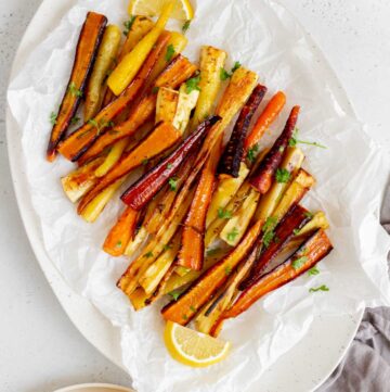 Overhead view of a platter of honey roasted parsnips and carrots with lemons on the side.