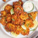 Overhead view of a plate of onion fritters with green onion and lemon wedges for garnish.