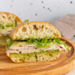 Two pesto turkey sandwiches on a wooden serving board.
