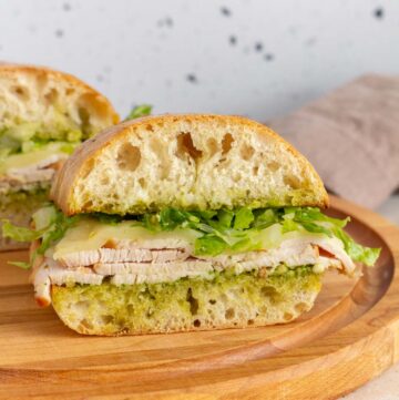 Two pesto turkey sandwiches on a wooden serving board.