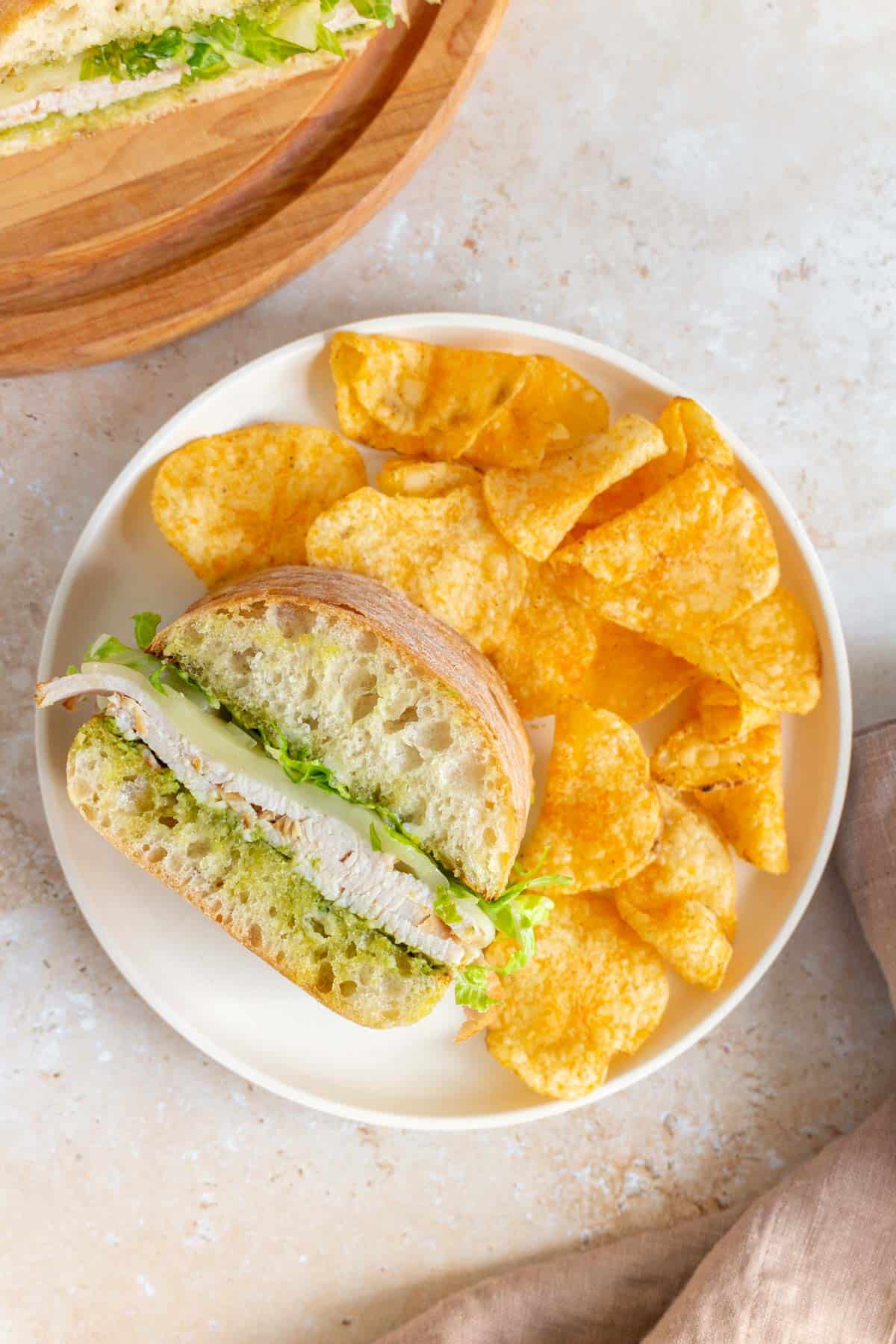 Overhead view of a serving of pesto turkey sandwich with chips on a plate.