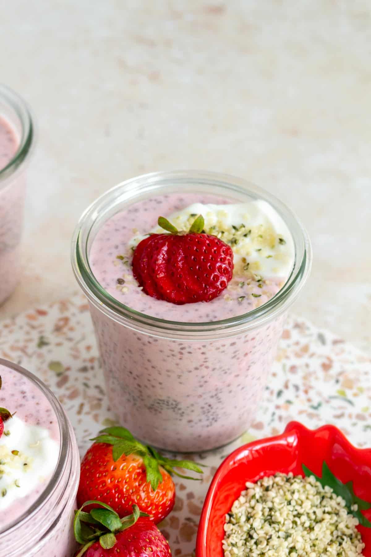 A jar of strawberry chia pudding with a cut strawberry, yogurt, and hemp hearts.