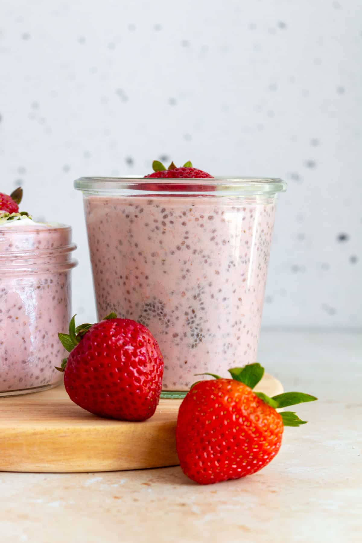 A jar of strawberry chia pudding with fresh strawberries in front.