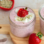 A slightly overhead angled view of a mason jar of strawberry chia pudding topped with strawberries, yogurt, and hemp hearts.