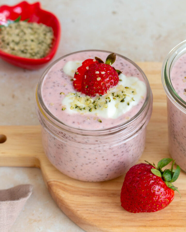 A slightly overhead angled view of a mason jar of strawberry chia pudding topped with strawberries, yogurt, and hemp hearts.