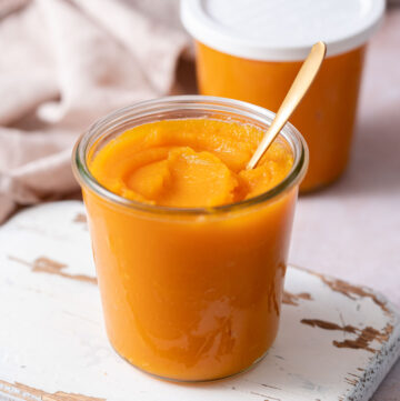 A jar of homemade pumpkin puree with a spoon inserted and a second jar in the back with a lid.