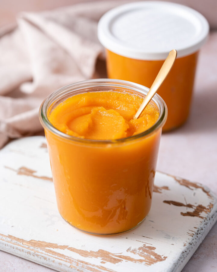 A jar of homemade pumpkin puree with a spoon inserted and a second jar in the back with a lid.