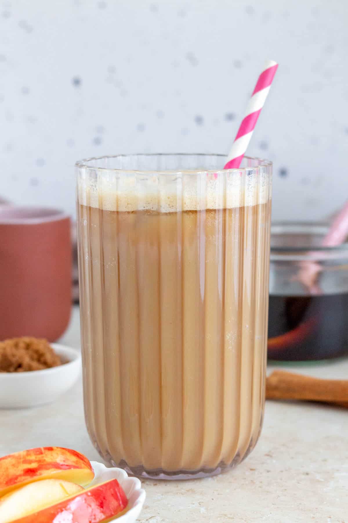 Profile view of a glass of iced apple crisp oat milk shaken espresso with a straw.