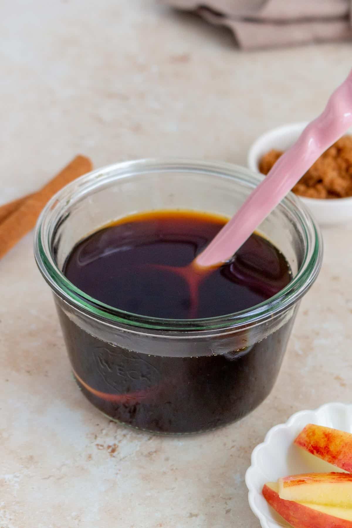 A jar of apple brown sugar syrup with a spoon inside.
