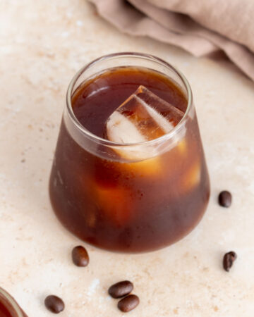 A glass of cold brew with ice. Coffee beans scattered around.