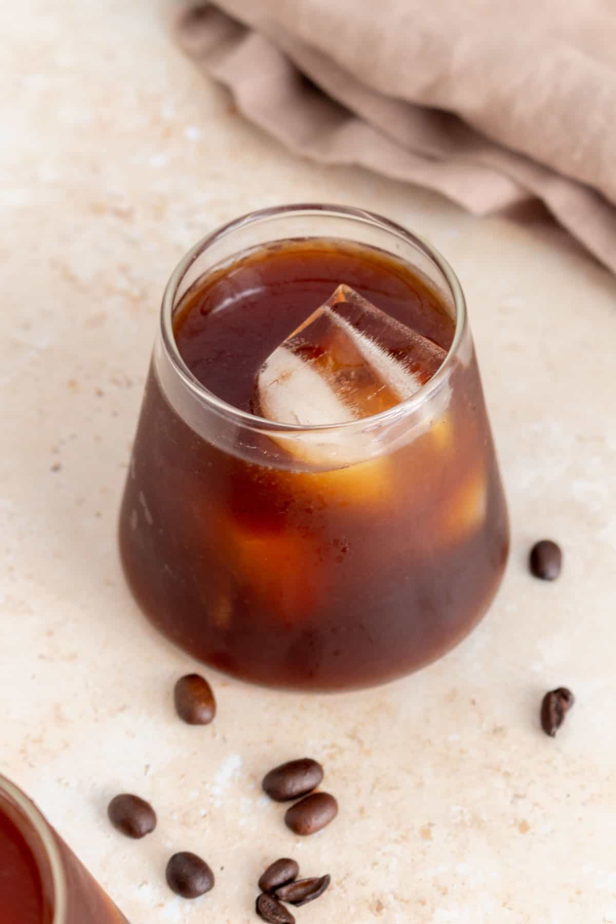 A glass of cold brew with ice. Coffee beans scattered around.