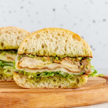 A profile view of a pesto chicken sandwich on a wooden serving board.