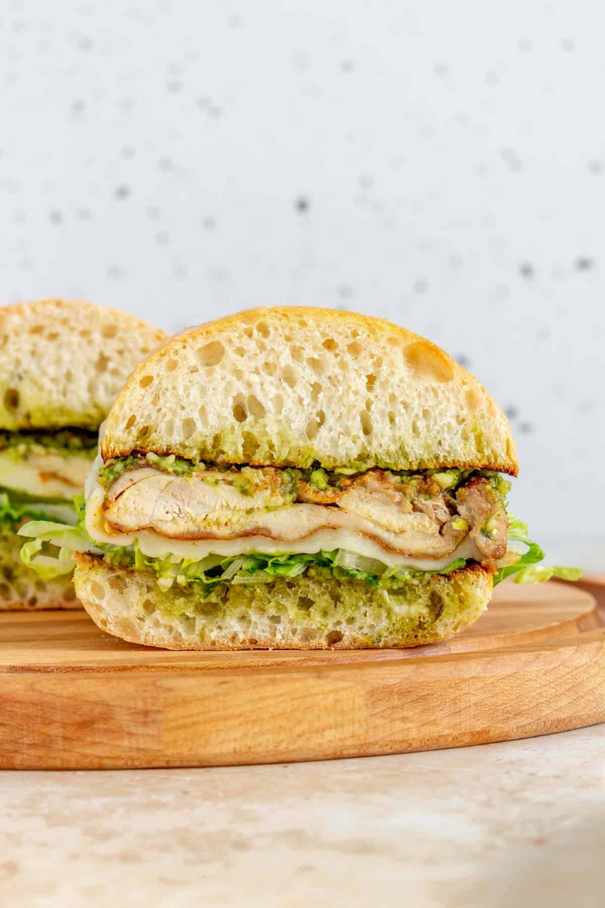 A profile view of a pesto chicken sandwich on a wooden serving board.