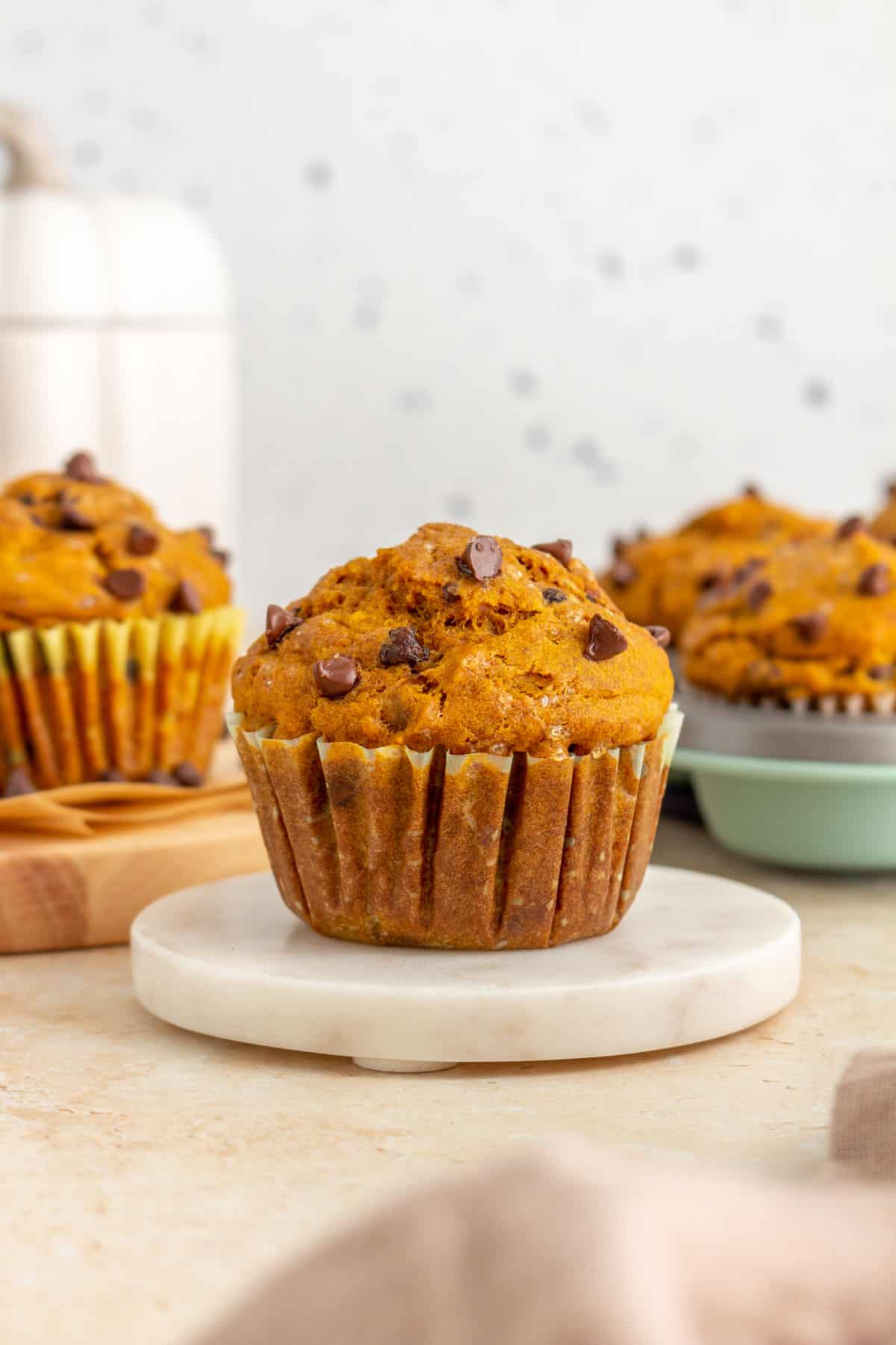 A pumpkin banana muffin on a marble coaster with more muffins in the background out of focus.