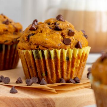 A pumpkin banana muffin surrounded by some scattered chocolate chips. A cup of coffee in the back.