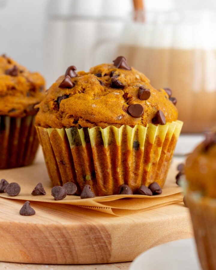 A pumpkin banana muffin surrounded by some scattered chocolate chips. A cup of coffee in the back.