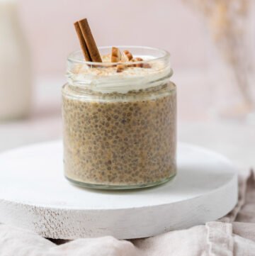 A jar of pumpkin chia pudding topped with pecans, yogurt, and a cinnamon stick.