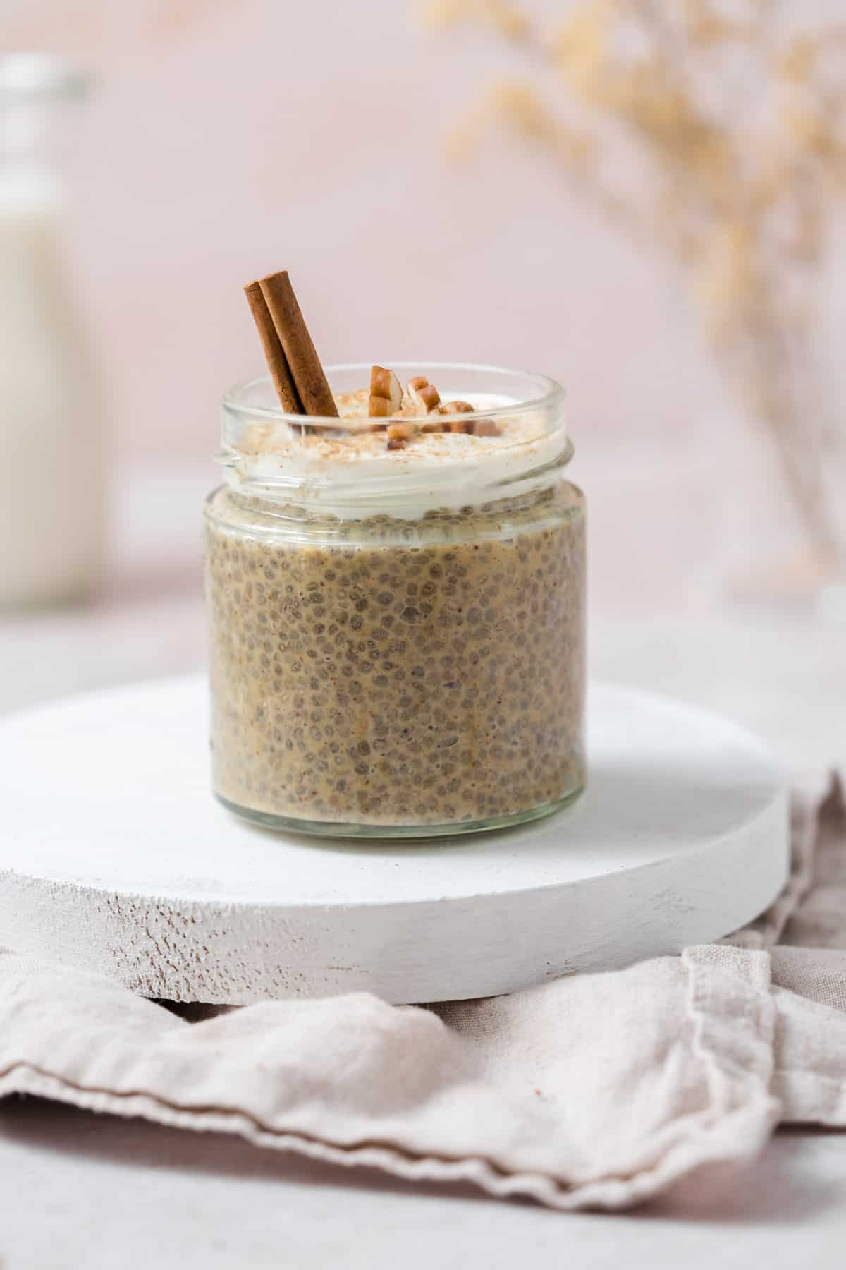 A jar of pumpkin chia pudding topped with pecans, yogurt, and a cinnamon stick.