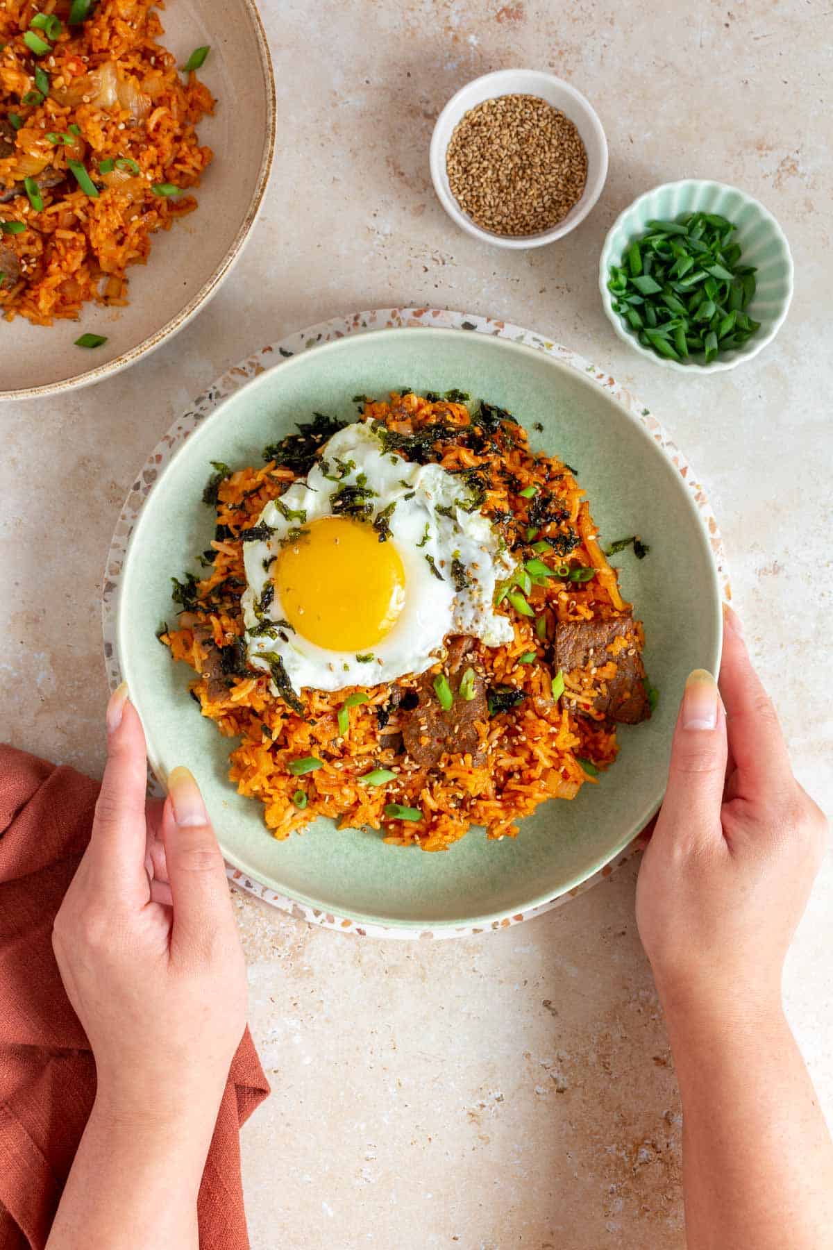 A plate of gochujang fried rice topped with seaweed and egg being held by a hand.