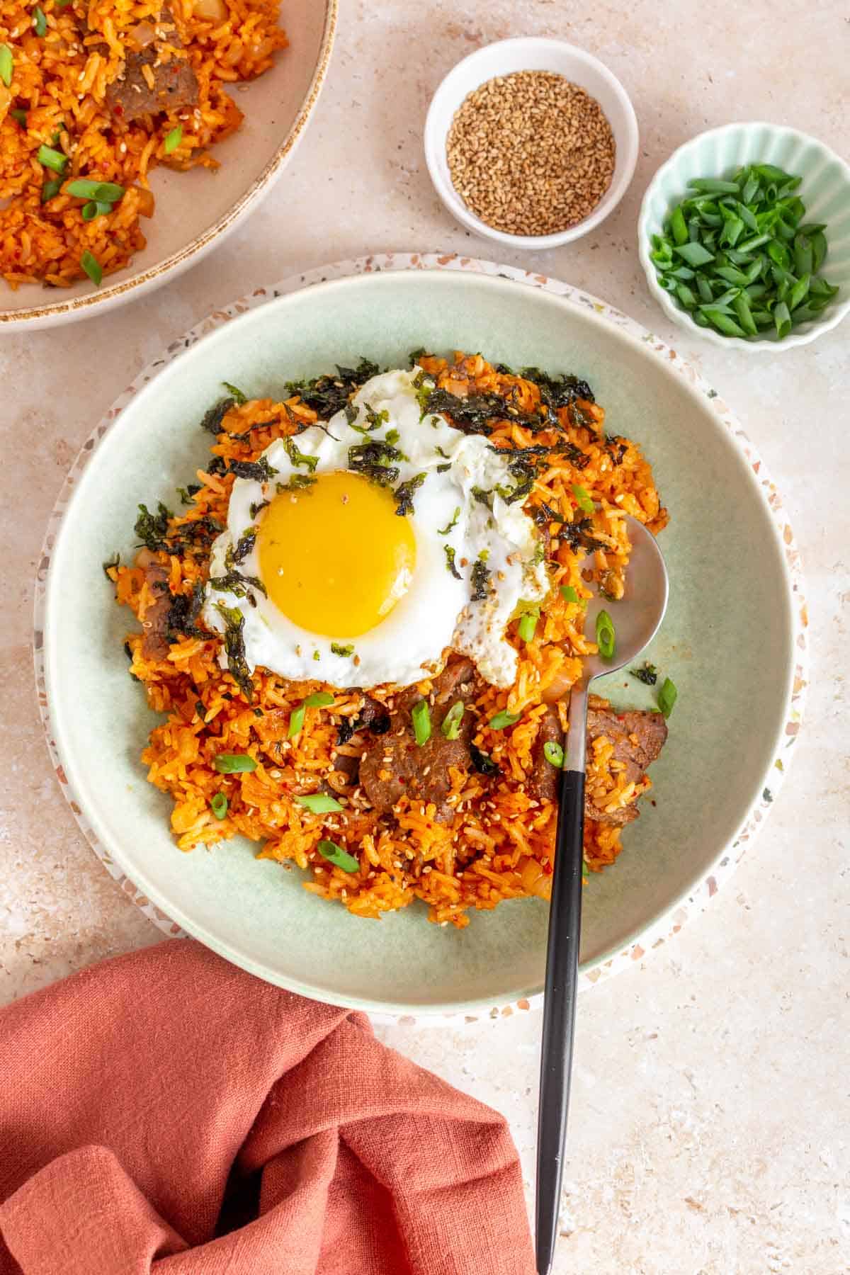 A plate of gochujang fried rice topped with seaweed and a fried egg with a spoon tucked into the rice.