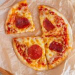 Overhead view of an air fryer tortilla pizza with pepperoni, cut into four.