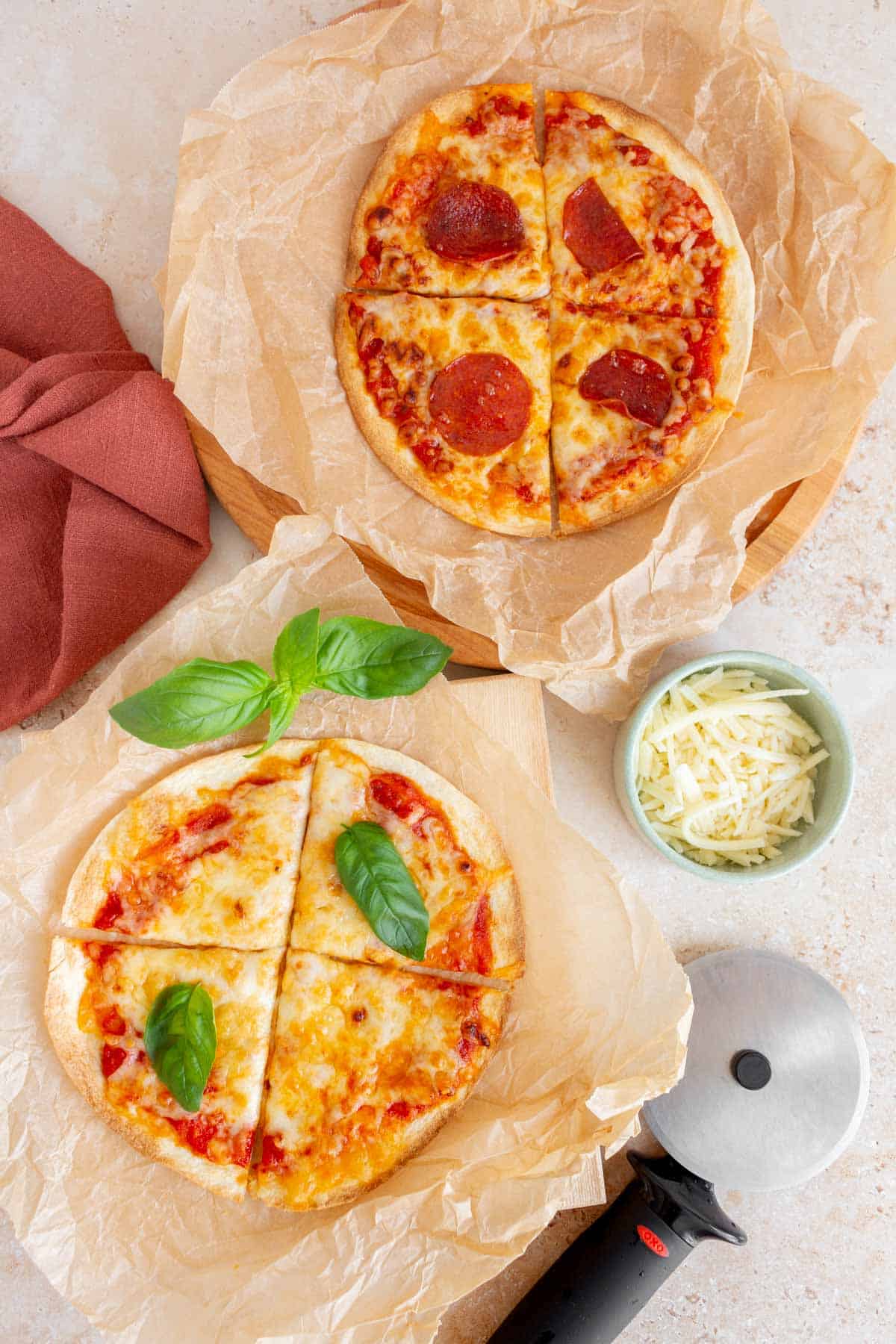 Two air fryer tortilla pizzas on wrinkly parchment paper.