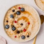 An overhead view of barley porridge in a bowl with maple syrup, berries, and granola.