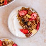 A bowl of yogurt with berry granola on top.